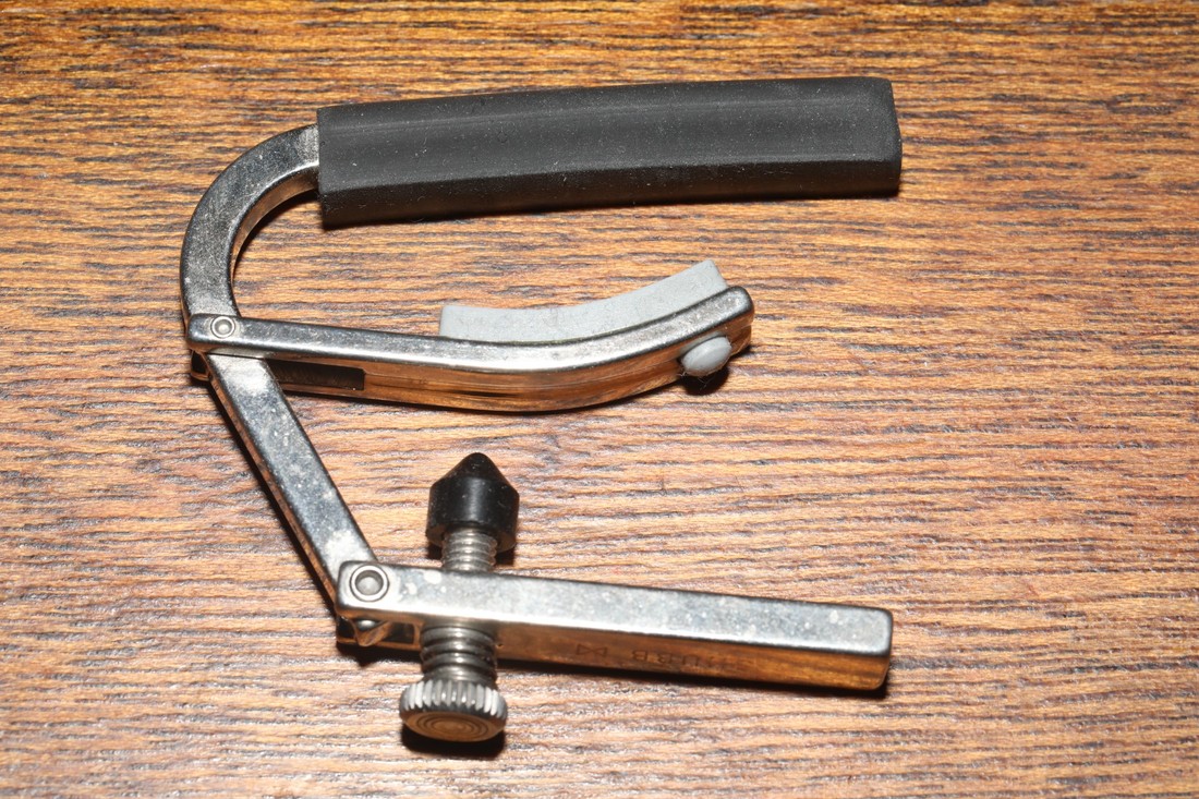 Chrome Shubb guitar capo photographed on a wooden surface.