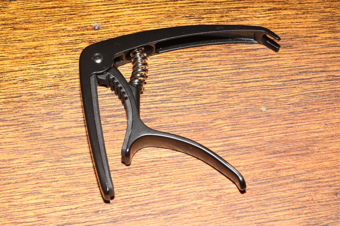 Black spring-style guitar capo photographed on a wooden surface.